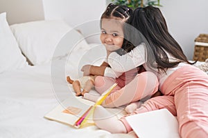 Adorable twin girls hugging each other sitting on bed at bedroom