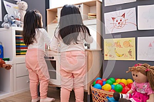 Adorable twin girls playing with play kitchen standing at kindergarten