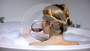 Adorable woman drinking wine in bath with foam bubbles, wellness and spa, relax