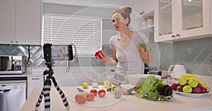 Adorable woman talking recording cooking video at kitchen interior. Beautiful young female blogger preparing healthy