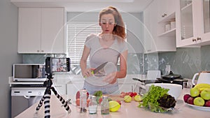 Adorable woman talking recording cooking video at kitchen interior. Beautiful young female blogger preparing healthy