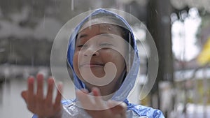 Adorable young asian girl in blue raincoat enjoy to play with the rain in front of the house.