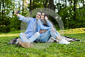 Adorable young couple man and woman sitting on green grass in park and taking selfie on smartphone