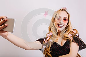 Adorable young girl with blonde long curly hair taking selfie at party, smiling to camera, covered with pink stars