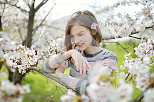 Adorable young girl in blooming cherry tree garden on beautiful spring day. Cute child picking fresh cherry tree flowers at spring