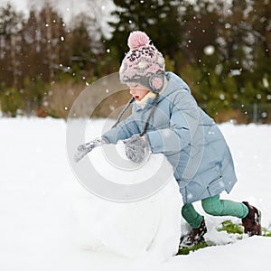 Adorable young girl building a snowman in the backyard. Cute child playing in a snow
