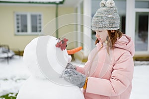 Adorable young girl building a snowman in the backyard. Cute child playing in a snow