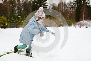 Adorable young girl building a snowman in the backyard. Cute child playing in a snow