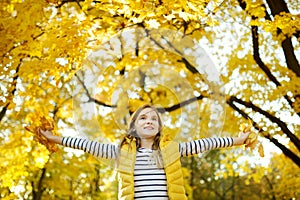 Adorable young girl having fun on beautiful autumn day. Happy child playing in autumn park. Kid gathering yellow fall foliage