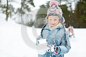 Adorable young girl having fun in beautiful winter park. Cute child playing in a snow. Winter activities for family with kids