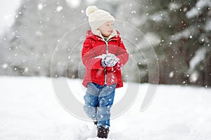 Adorable young girl having fun in beautiful winter park during snowfall. Cute child playing in a snow