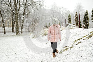 Adorable young girl having fun in beautiful winter park during snowfall. Cute child playing in a snow
