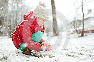 Adorable young girl having fun in beautiful winter park during snowfall. Cute child playing in a snow