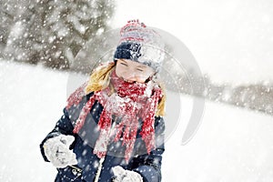 Adorable young girl having fun in beautiful winter park during snowfall. Cute child playing in a snow