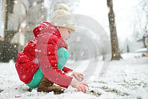 Adorable young girl having fun in beautiful winter park during snowfall. Cute child playing in a snow