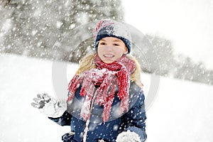 Adorable young girl having fun in beautiful winter park during snowfall. Cute child playing in a snow