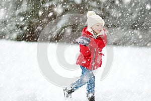 Adorable young girl having fun in beautiful winter park during snowfall. Cute child playing in a snow