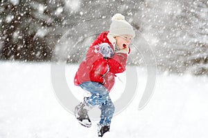 Adorable young girl having fun in beautiful winter park during snowfall. Cute child playing in a snow