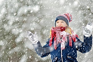 Adorable young girl having fun in beautiful winter park during snowfall. Cute child playing in a snow