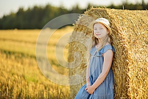 Adorable young girl having fun in a wheat field on a summer day. Child playing at hay bale field during harvest time. Kid enjoying