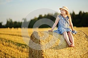Adorable young girl having fun in a wheat field on a summer day. Child playing at hay bale field during harvest time. Kid enjoying