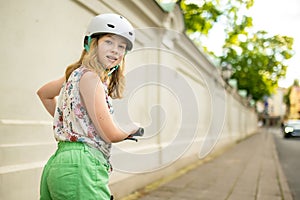 Adorable young girl riding her scooter in a city on sunny summer evening. Pretty preteen child riding a roller. Active leisure and