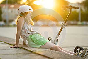Adorable young girl riding her scooter in a city on sunny summer evening. Pretty preteen child riding a roller. Active leisure and