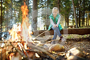 Adorable young girl roasting marshmallows on stick at bonfire. Child having fun at camp fire. Camping with children in fall forest