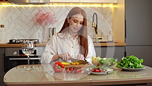 Adorable young redhead woman blogger shooting video food blog about cooking on camera of phone at table in kitchen.