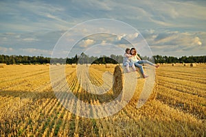 Adorable young sisters having fun in a wheat field on a summer day. Children playing at hay bale field during harvest time. Kids