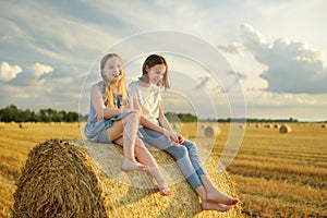 Adorable young sisters having fun in a wheat field on a summer day. Children playing at hay bale field during harvest time. Kids