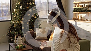 An adorable young woman adjusting a virtual reality headset near a Christmas tree.