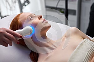Adorable young woman enjoying electric microcurrent massage photo