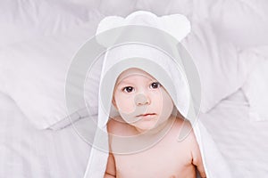 Adorably baby lie on white towel in bed. Happy childhood and healthcare concept.