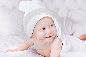 Adorably baby lie on white towel in bed. Happy childhood and healthcare concept.