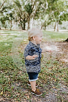 Adorable šťastný a roztomilý malý kaukazský batoľa dieťa chlapec dlho vlasy usmievavý, a beh mimo v zelený 