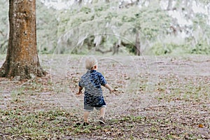 Adorably Happy and Cute Little Caucasian Toddler Baby Boy with Long Blond Hair Laughing, Playing, and Running Outside in Green Nat