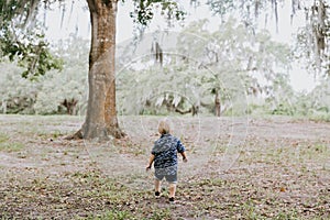 Adorably Happy and Cute Little Caucasian Toddler Baby Boy with Long Blond Hair Laughing, Playing, and Running Outside in Green Nat