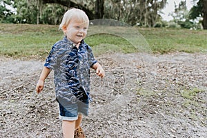 Adorably Happy and Cute Little Caucasian Toddler Baby Boy with Long Blond Hair Laughing, Playing, and Running Outside in Green Nat