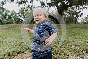 Adorably Happy and Cute Little Caucasian Toddler Baby Boy with Long Blond Hair Laughing, Playing, and Running Outside in Green Nat