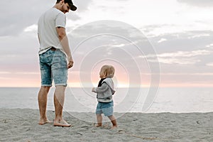 Adorably Perfect Young Father and Baby Toddler Son Family Having Fun Time at the Sandy Beach During Sunset Outside By the Ocean Wa