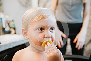 Adorably Precious Cute Little Blond Toddler Boy Showing Off His New Hair Style after Getting His First Hair Cut and Eating Candy