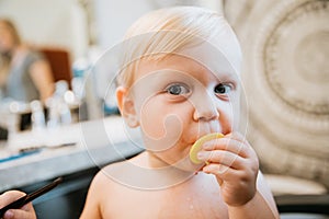 Adorably Precious Cute Little Blond Toddler Boy Showing Off His New Hair Style after Getting His First Hair Cut and Eating Candy