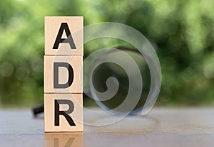 ADR Abbreviation On Wooden  Blocks on table with magnifier on green background