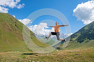 Adrenaline Rush: A Man in an Orange T-Shirt Jumps against Green Mountains