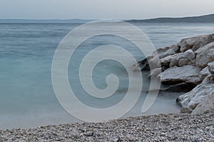 Adriatic seascape, pebble beach and rocks, hazy silhouettes of islands in distance at dusk