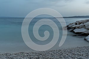 Adriatic seascape, pebble beach and rocks, hazy silhouettes of islands in distance at dusk