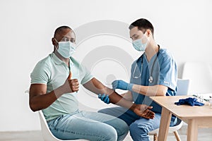 Adult african american guy approving procedure, gets covid vaccine in clinic, male nurse injecting into shoulder photo