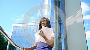 Adult african american young businesswoman works with documents near modern office building