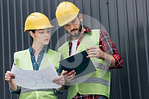 adult architects in hardhats working with blueprint and clipboard